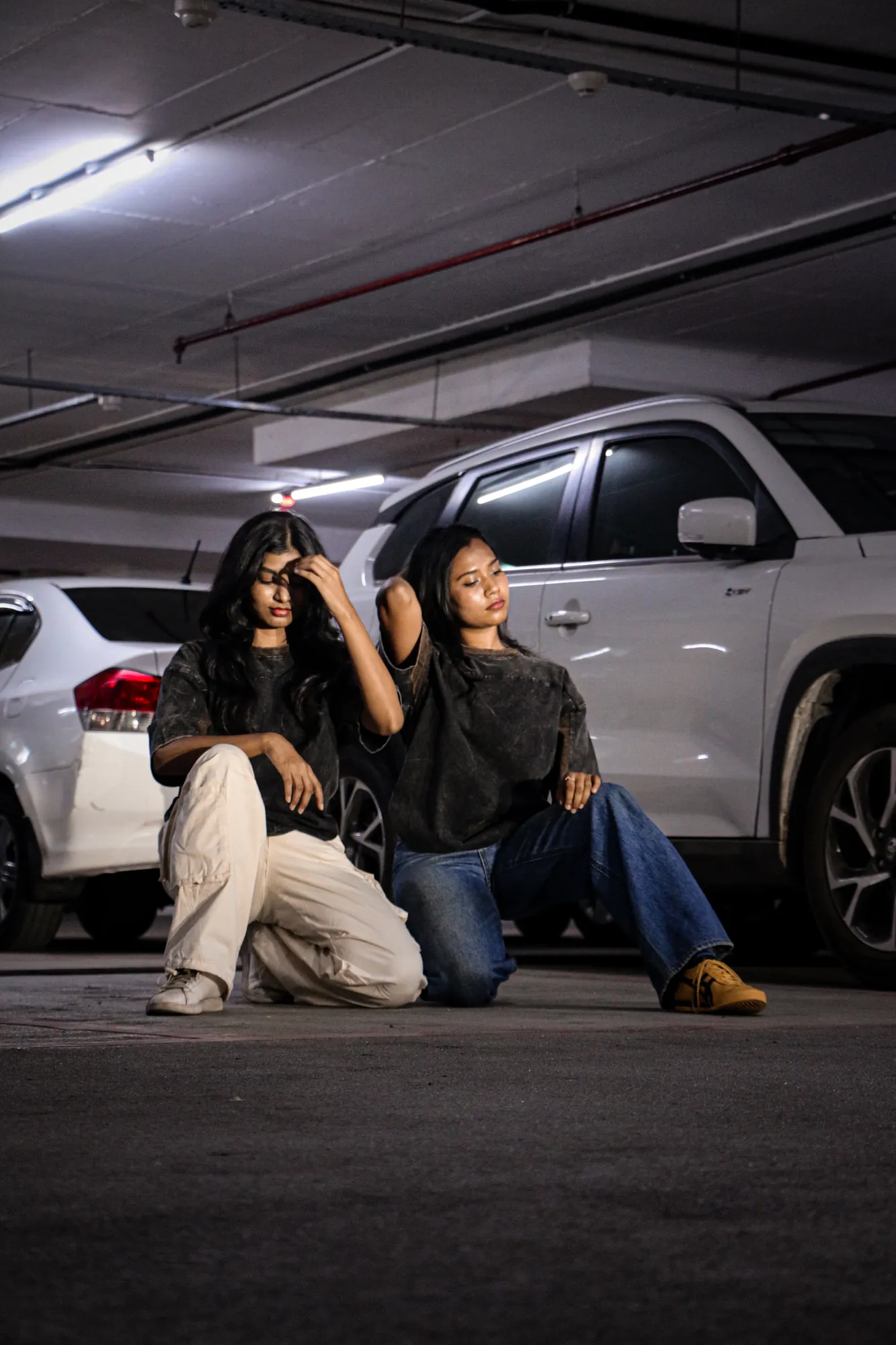 Two people wearing The ORIGIN tee, seated beside a car at night